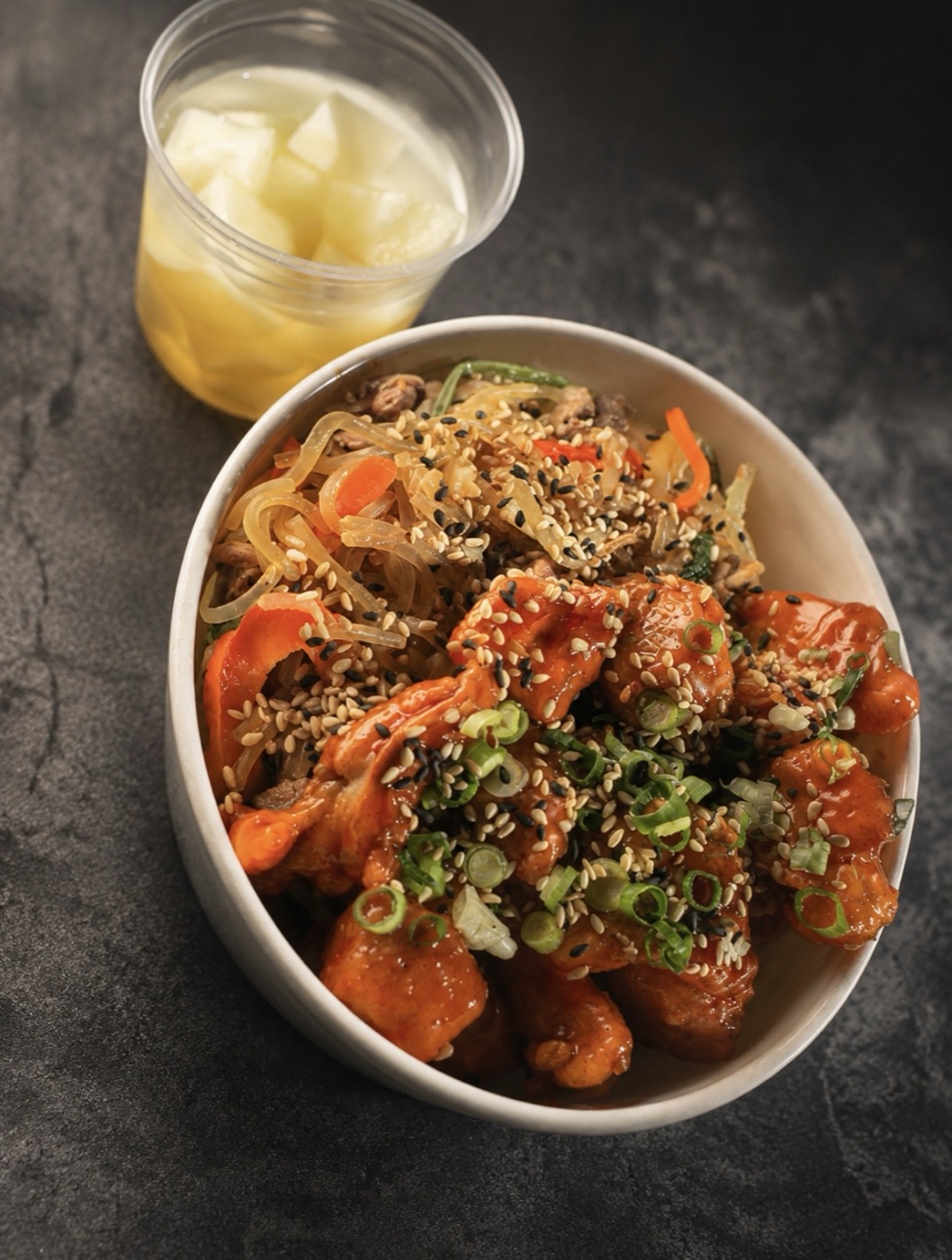 A bowl of saucy Korean fried chicken over glass noodles, topped with sesame and spring onion